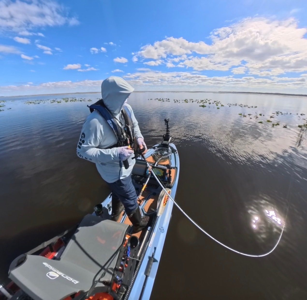 Eric Dudash standing in his fishing kayak on open water under a wide blue sky, casting